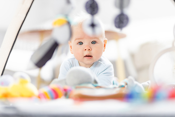 Image showing Cute baby boy playing with hanging toys arch on mat at home Baby activity and play center for early infant development. Baby playing at home