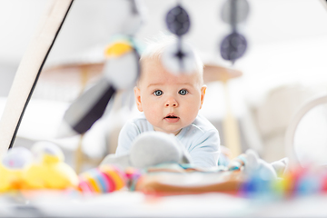 Image showing Cute baby boy playing with hanging toys arch on mat at home Baby activity and play center for early infant development. Baby playing at home