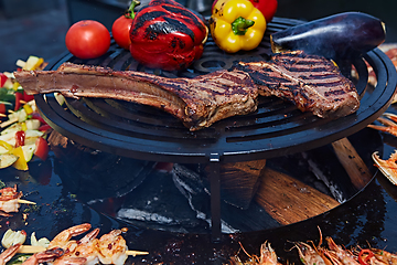 Image showing Tomahawk rib beef steak and T-bone on hot black grill.