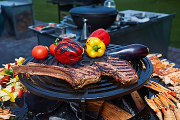 Image showing Tomahawk rib beef steak and T-bone on hot black grill.