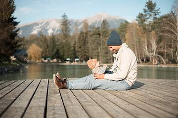 Image showing Happy family. Father playing with her baby boy infant oudoors on sunny autumn day. Portrait of dad and little son on wooden platform by lake. Positive human emotions, feelings, joy.