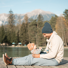 Image showing Happy family. Father playing with her baby boy infant oudoors on sunny autumn day. Portrait of dad and little son on wooden platform by lake. Positive human emotions, feelings, joy.
