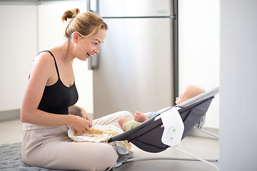 Image showing Happy smiling mother playing with her little baby son sitting in electric rocking chair at home. Child development and happy parenting.