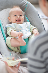 Image showing Mother spoon feeding her baby boy infant child in baby chair with fruit puree. Baby solid food introduction concept.