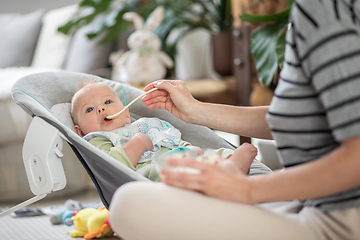 Image showing Mother spoon feeding her baby boy infant child in baby chair with fruit puree. Baby solid food introduction concept.