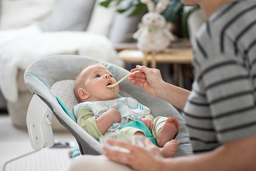 Image showing Mother spoon feeding her baby boy infant child in baby chair with fruit puree. Baby solid food introduction concept.