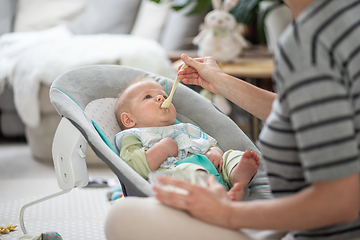 Image showing Mother spoon feeding her baby boy infant child in baby chair with fruit puree. Baby solid food introduction concept.