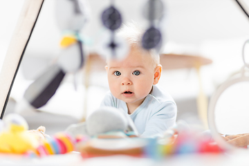 Image showing Cute baby boy playing with hanging toys arch on mat at home Baby activity and play center for early infant development. Baby playing at home