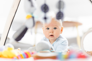 Image showing Cute baby boy playing with hanging toys arch on mat at home Baby activity and play center for early infant development. Baby playing at home