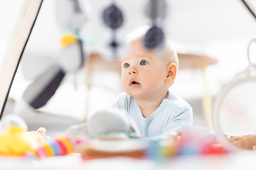 Image showing Cute baby boy playing with hanging toys arch on mat at home Baby activity and play center for early infant development. Baby playing at home