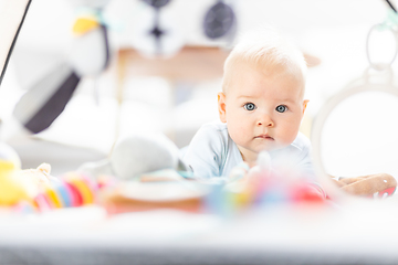 Image showing Cute baby boy playing with hanging toys arch on mat at home Baby activity and play center for early infant development. Baby playing at home