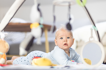 Image showing Cute baby boy playing with hanging toys arch on mat at home Baby activity and play center for early infant development. Baby playing at home