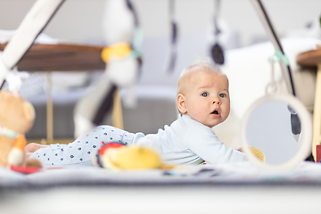 Image showing Cute baby boy playing with hanging toys arch on mat at home Baby activity and play center for early infant development. Baby playing at home