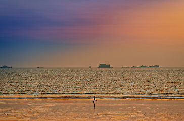 Image showing Athlete runs along the sandy shore of the ocean at sunset