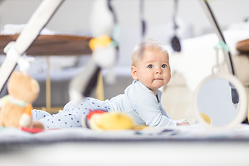 Image showing Cute baby boy playing with hanging toys arch on mat at home Baby activity and play center for early infant development. Baby playing at home