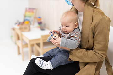 Image showing Mother holding infant baby boy in her lap, sitting and waiting in front of doctor's office for pediatric well check. child's health care concept