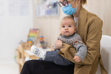 Image showing Mother holding infant baby boy in her lap, sitting and waiting in front of doctor's office for pediatric well check. child's health care concept