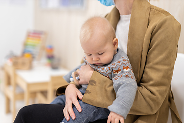 Image showing Mother holding infant baby boy in her lap, sitting and waiting in front of doctor's office for pediatric well check. child's health care concept