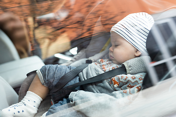 Image showing Cute little baby boy sleeping strapped into infant car seat in passenger compartment during car drive.