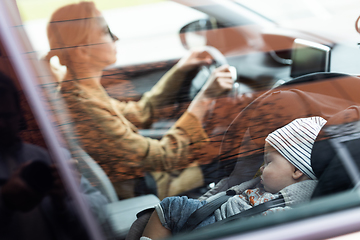 Image showing Mother concentrating on driving family car running errands while her baby sleeps in infant car seat by her site.