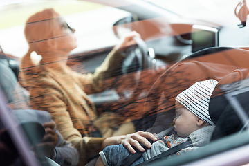 Image showing Mother concentrating on driving family car running errands while her baby sleeps in infant car seat by her site.