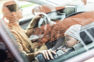 Image showing Mother concentrating on driving family car running errands while her baby sleeps in infant car seat by her site.