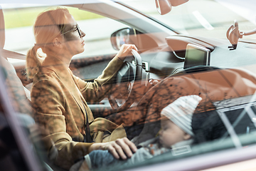 Image showing Mother concentrating on driving family car running errands while her baby sleeps in infant car seat by her site.