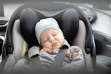 Image showing Cute little baby boy sleeping strapped into infant car seat in passenger compartment during car drive.