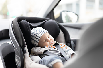 Image showing Cute little baby boy sleeping strapped into infant car seat in passenger compartment during car drive.