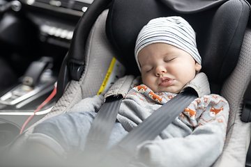 Image showing Cute little baby boy sleeping strapped into infant car seat in passenger compartment during car drive.