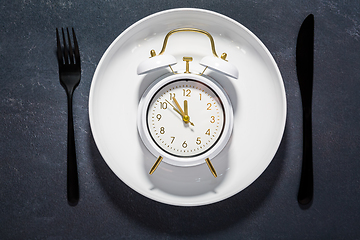 Image showing White plate and clock on a dark background with copy space. Concept of interval fasting and autophagy.