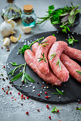 Image showing Raw sausages on slate, with herbs and spices, prepared for grill and BBQ