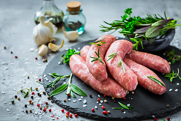 Image showing Raw sausages on slate, with herbs and spices, prepared for grill