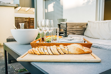 Image showing Freshly baked baguette with healthy snack and glasses on terrace or patio