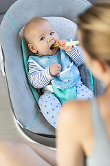 Image showing Mother spoon feeding her baby boy infant child in baby chair with fruit puree. Baby solid food introduction concept.