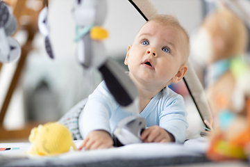 Image showing Cute baby boy playing with hanging toys arch on mat at home Baby activity and play center for early infant development. Baby playing at home