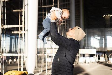 Image showing Father happily holding and lifting his infant baby boy child in the air after being rejunited in front of airport terminal station. Baby travel concept.