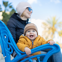 Image showing Young mother with her cute infant baby boy child on bench in city park.