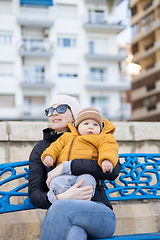 Image showing Young mother with her cute infant baby boy child on bench in city park.