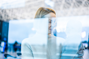 Image showing Thoughtful young mother looking trough window holding his infant baby boy child while waiting to board an airplane at airport terminal departure gates. Travel with baby concept.