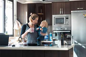 Image showing Happy mother and little infant baby boy together making pancakes for breakfast in domestic kitchen. Family, lifestyle, domestic life, food, healthy eating and people concept.