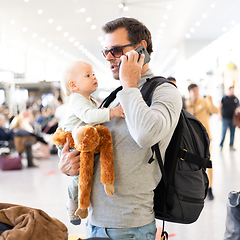 Image showing Father traveling with child, holding his infant baby boy at airport terminal waiting to board a plane. Travel with kids concept.