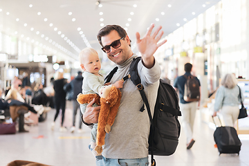 Image showing Father traveling with child, holding his infant baby boy at airport terminal waiting to board a plane waving goodby. Travel with kids concept.