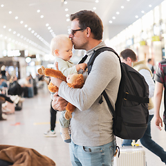 Image showing Father traveling with child, holding his infant baby boy at airport terminal waiting to board a plane. Travel with kids concept.