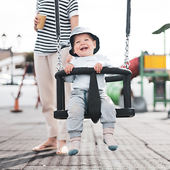 Image showing Mother pushing her infant baby boy child on a swing on playground outdoors.