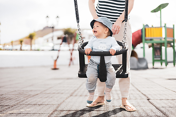 Image showing Mother pushing her infant baby boy child on a swing on playground outdoors.