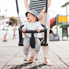 Image showing Mother pushing her infant baby boy child on a swing on playground outdoors.