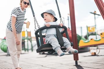 Image showing Mother pushing her infant baby boy child on a swing on playground outdoors.