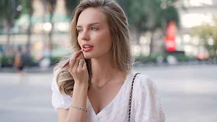 Image showing Young woman in summer dress fixes makeup outdoors