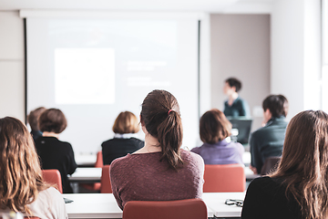 Image showing Female speaker giving presentation in lecture hall at university workshop . Participants listening to lecture and making notes. Scientific conference event